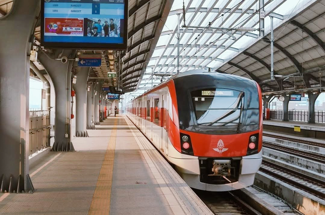A Red Line train arrives at the station as the digital signage screen displays the live schedule to Rangsit.