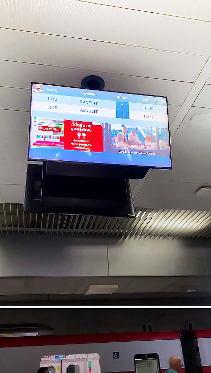A close-up of the station screen showing live train schedules to Rangsit for passengers waiting on the platform.