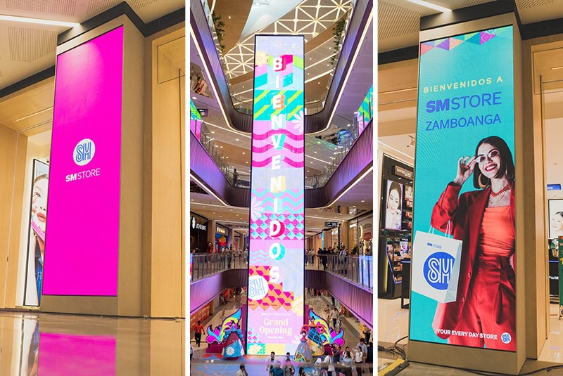 柱面の縦型 LED から吹き抜けの多層バナーまで、SM Store エリアでブランド訴求、二言語のウェルカム、キャンペーンビジュアルをライン全体に展開。