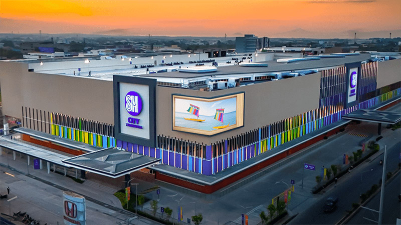 ยามพลบค่ำ SM City Zamboanga สว่างไสวด้วยแสงไฟ — ผนัง LED โค้งภายนอกและการเปิดไฟทั้งตัวอาคารสร้างจุดแลนด์มาร์คที่มองเห็นได้ทั่วเมือง โดยได้รับการสนับสนุนจากเครือข่ายดิจิทัลไซน์ที่ควบคุมแบบรวมศูนย์จาก CAYIN